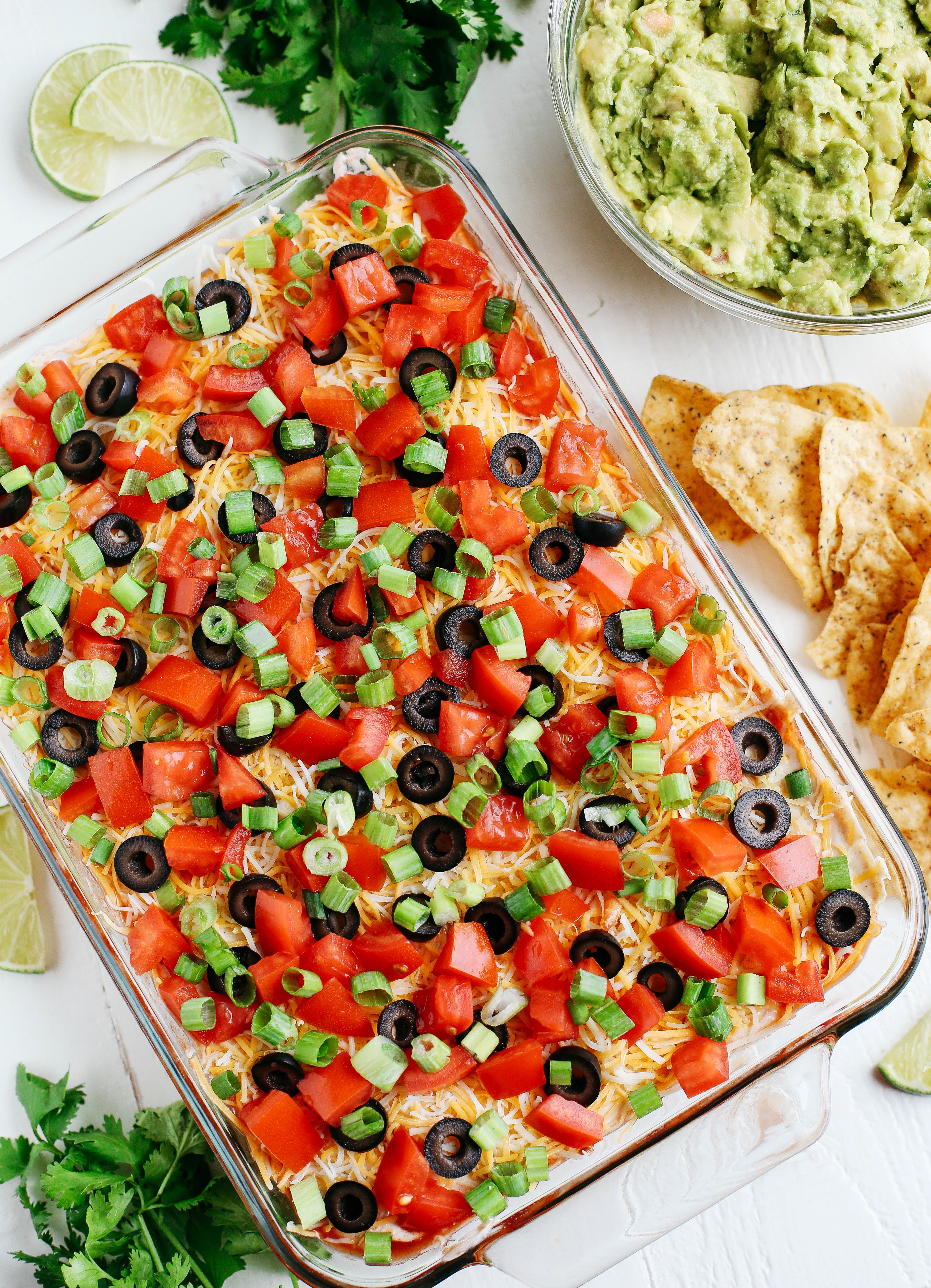 Healthier 7 Layer Spicy Taco Dip made with Greek yogurt, hummus, fresh guacamole, chunky salsa, homemade taco seasoning and all the fun toppings!  Super easy to make and always a crowdpleaser!