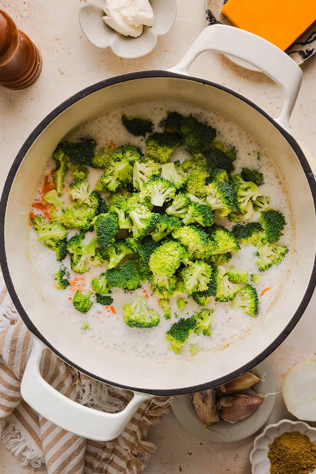 Broccoli added to creamy broccoli cheddar soup on the stove.