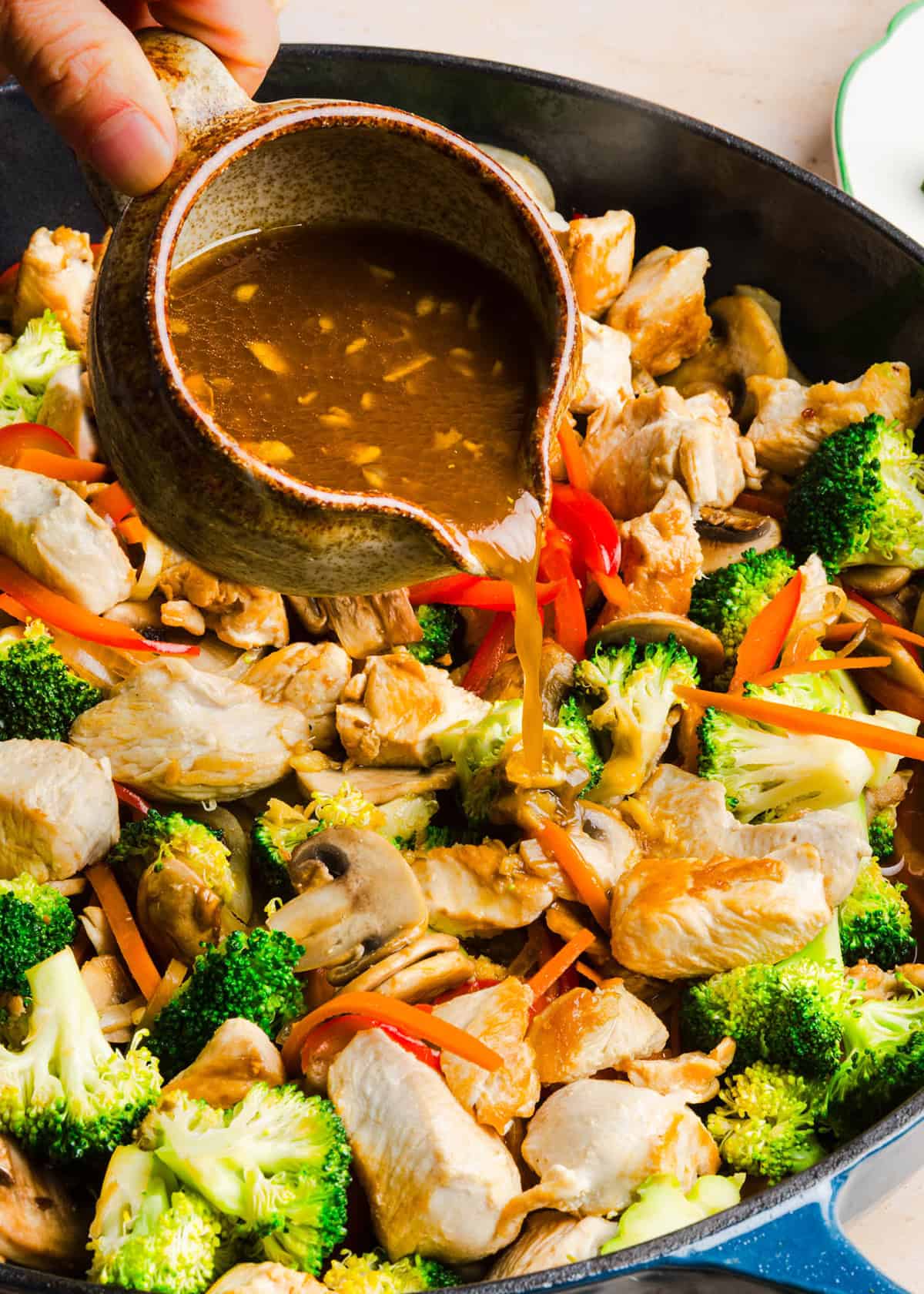 Homemade teriyaki sauce poured over chicken and vegetables in a skillet