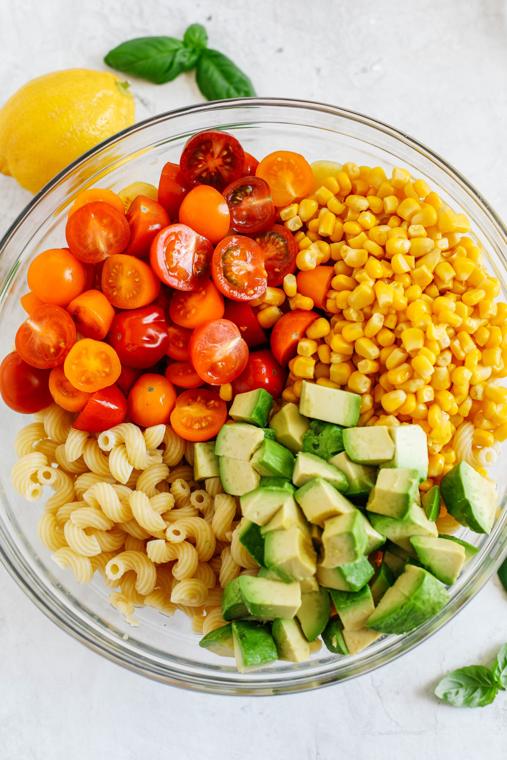 This EASY 10-minute Summer Pesto Pasta Salad is loaded with fresh ingredients like juicy tomatoes, corn, avocado, garlic, and lemon zest, all tossed together with warm pasta and delicious basil pesto!