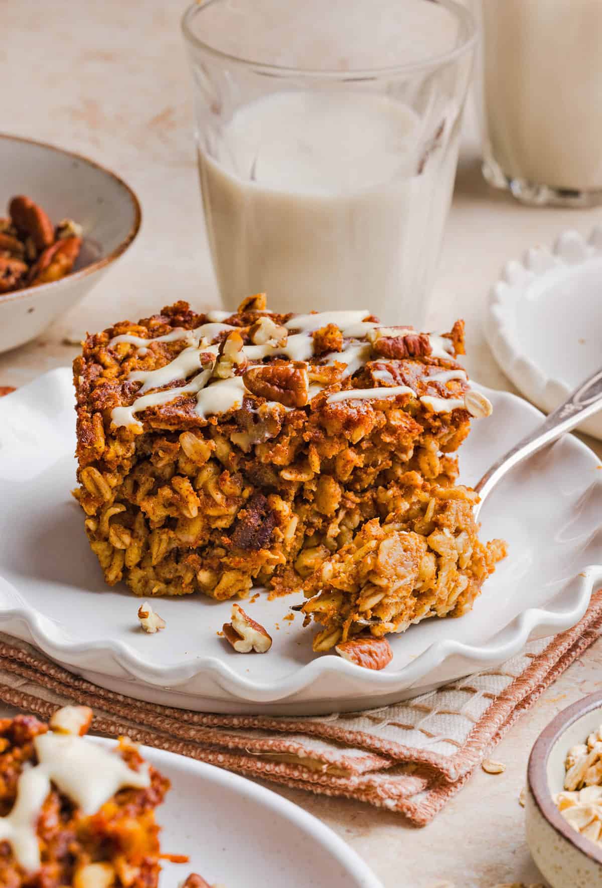A slice of pumpkin baked oatmeal topped with chopped pecans and maple cream cheese glaze served on a plate.
