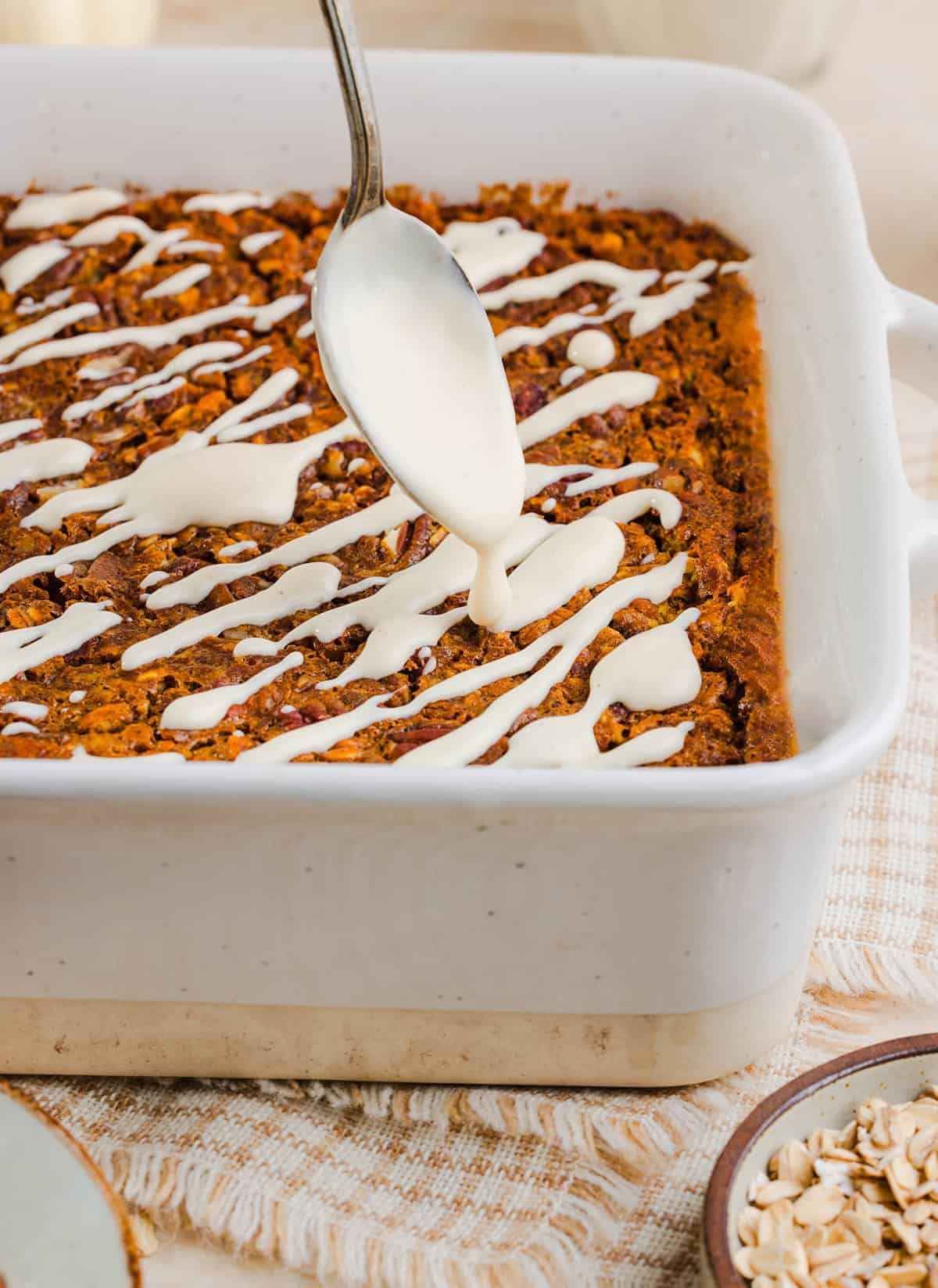 Pumpkin baked oatmeal drizzled with maple cream cheese glaze in a square baking dish.