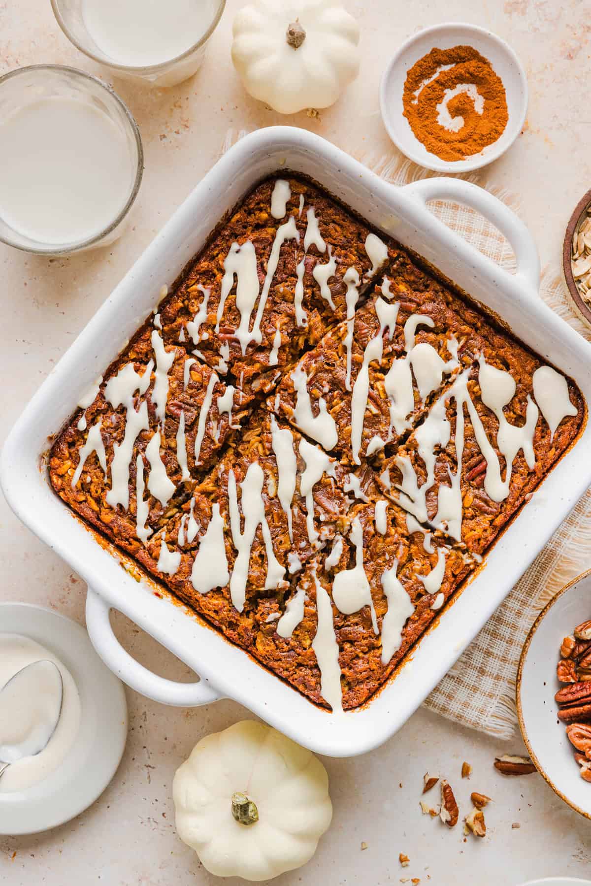 Pumpkin baked oatmeal topped with chopped pecans and maple cream cheese glaze in a square baking dish.