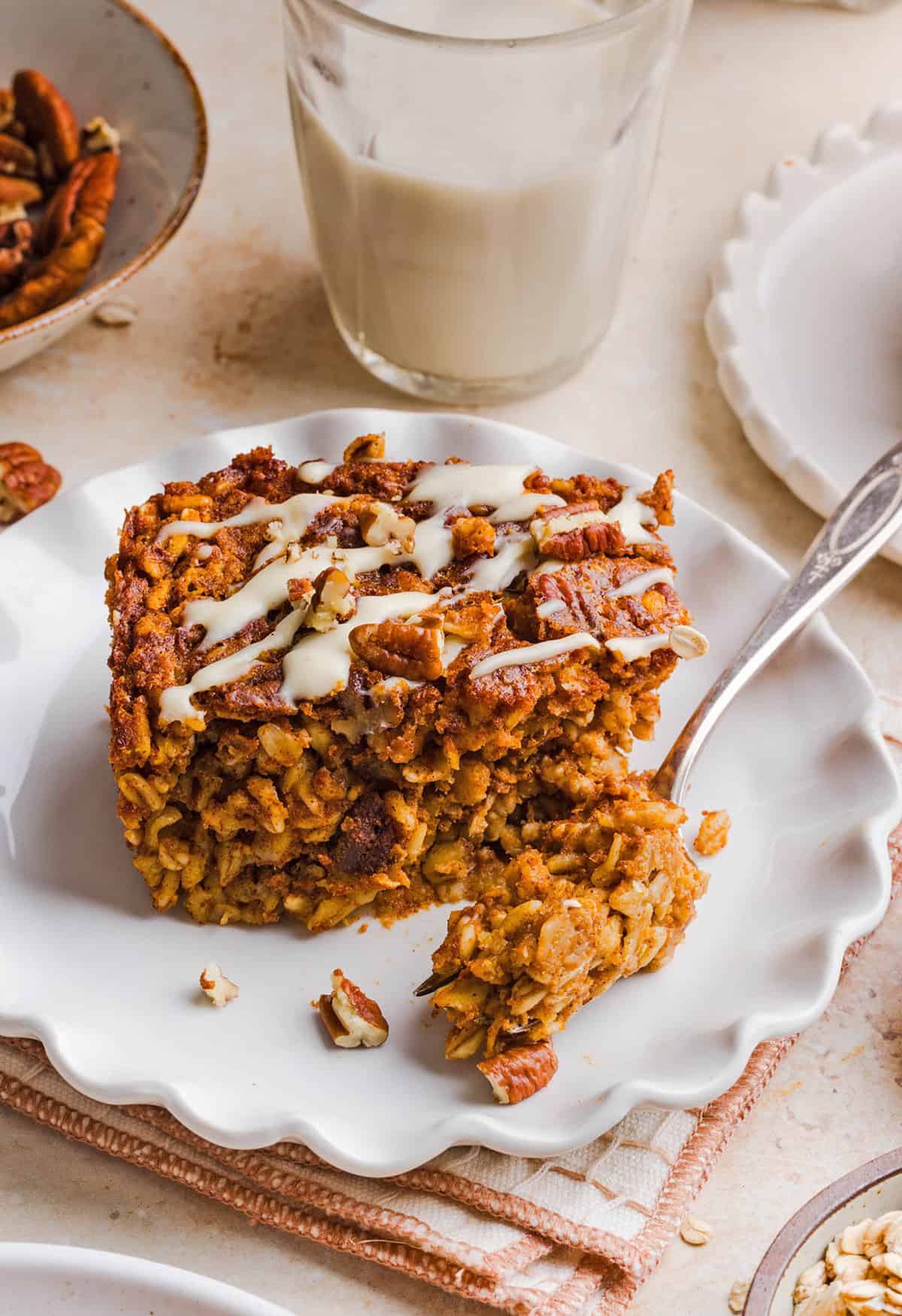 A slice of pumpkin baked oatmeal topped with chopped pecans and maple cream cheese glaze served on a plate.